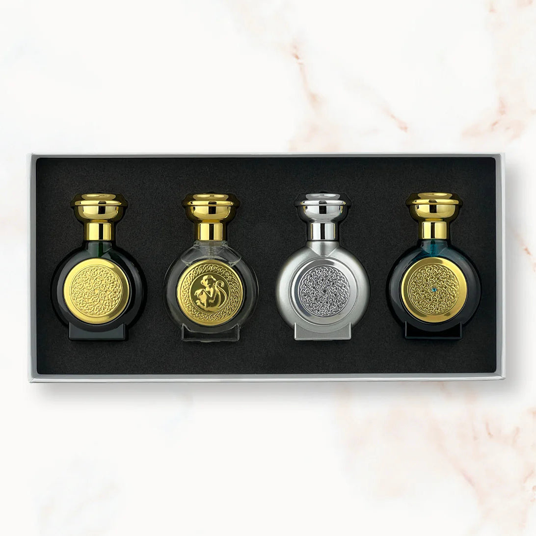 Set of four perfume bottles with gold and silver designs in a black box on a light marble background