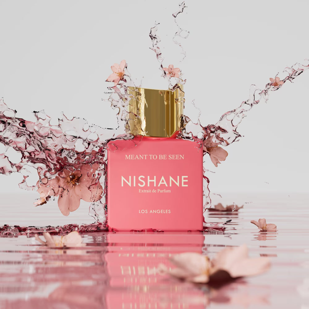 Nishane perfume bottle with pink label and gold cap on a reflective surface with floral elements.