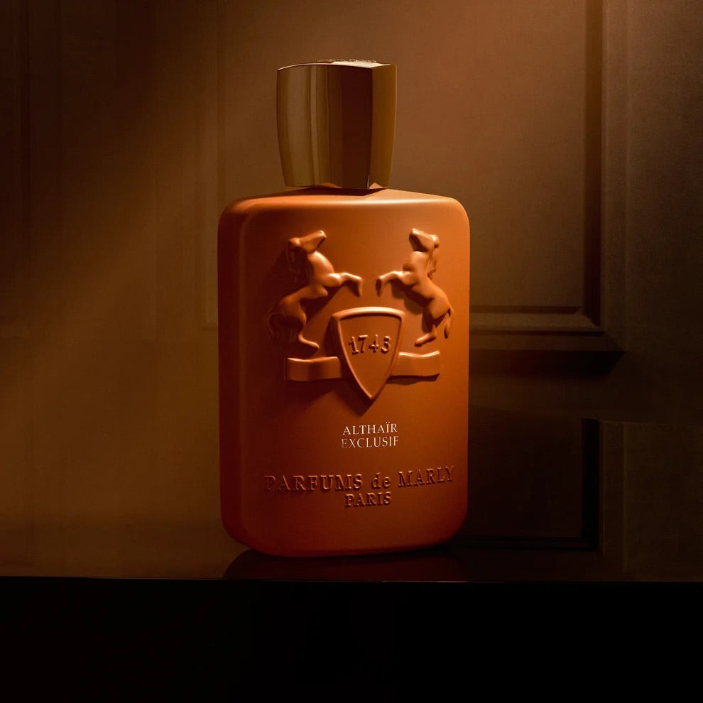 A rectangular perfume bottle with a metallic gold cap, featuring embossed horse and shield crest details on a warm brown background.