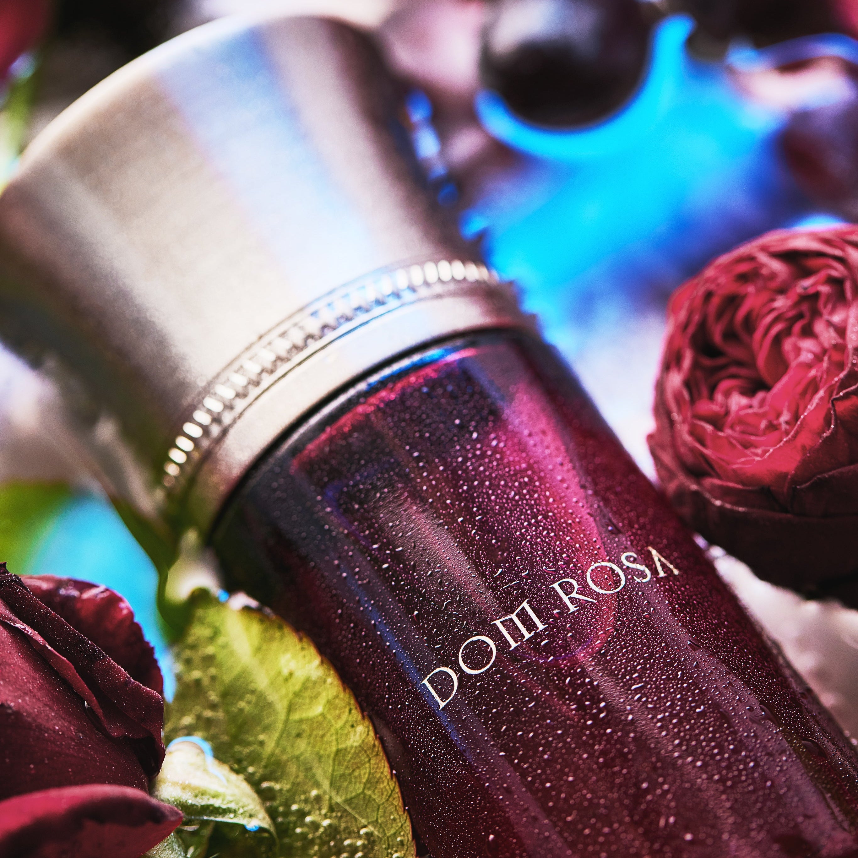 Bottle of Domi Rosa perfume with red roses and berries in the background