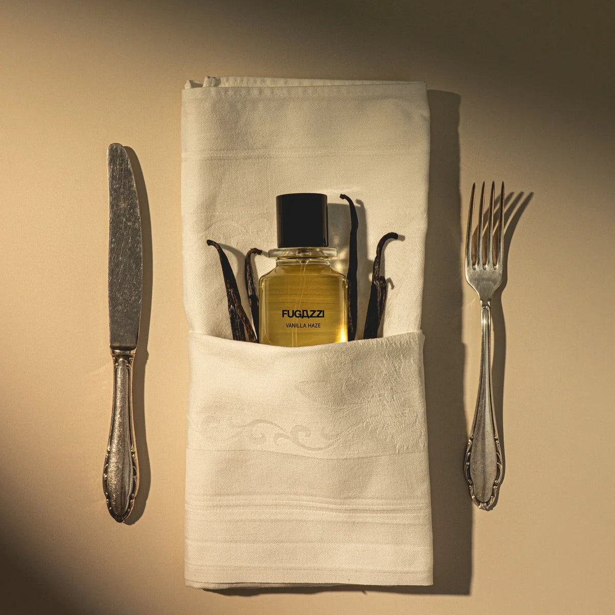Fragrance bottle with a cloth pouch, knife, and fork on a beige background