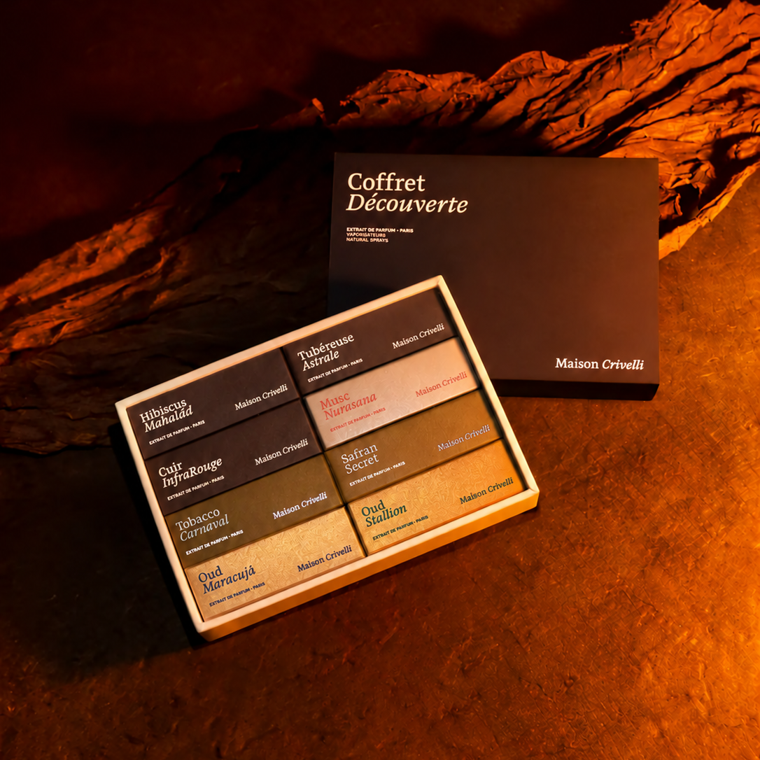 A boxed set of Maison Crivelli coffee blends displayed on a textured surface with dramatic warm lighting. The set includes both the outer black presentation box labeled 'Coffret Découvertes' and an open tray showing multiple coffee flavor blocks in dark, medium, and light tones.