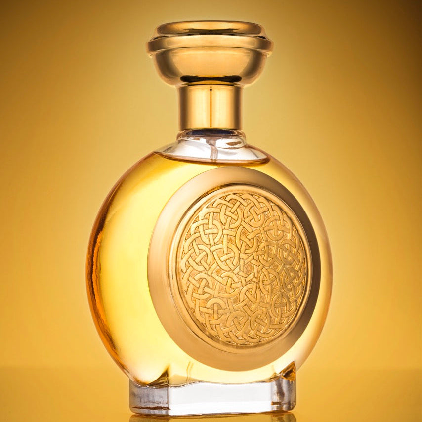 A round glass bottle with a stopper, filled with golden amber liquid, featuring an embossed circular pattern on the front. The bottle is centered against a warm golden gradient background with a soft reflection below.